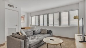 Una sala de estar moderna con un sofá gris, una mesa de centro redonda y un escritorio con una lámpara.