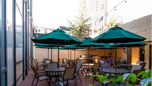 Un patio al aire libre con mesas y sillas, sombrillas verdes y una zona de barbacoa.