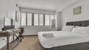 Una habitación de hotel moderna con una cama grande, un escritorio con computadora, un televisor y una ventana con persianas.