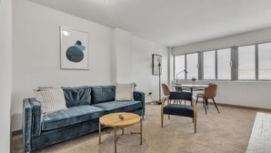 Una sala de estar moderna con un sofá azul, una mesa de centro redonda y una zona de comedor con mesa y sillas.