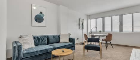 A modern living room with a blue sofa, a round coffee table, and a dining area with a table and chairs.
