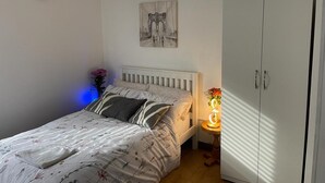 Un dormitorio con una cama, una mesita de noche con lámpara, un armario, un reloj y una obra de arte en la pared.
