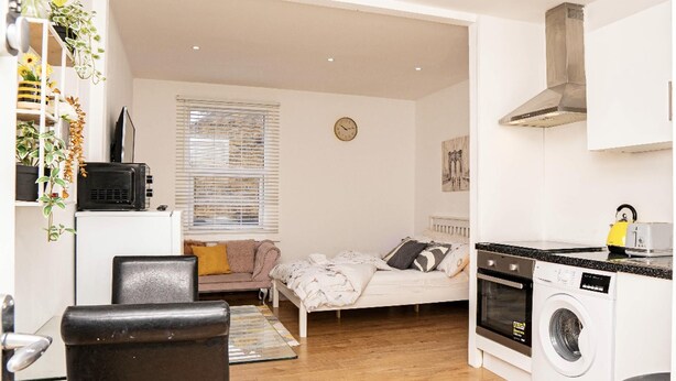 Un espacio habitable pequeño con cama, kitchenette y lavadora.