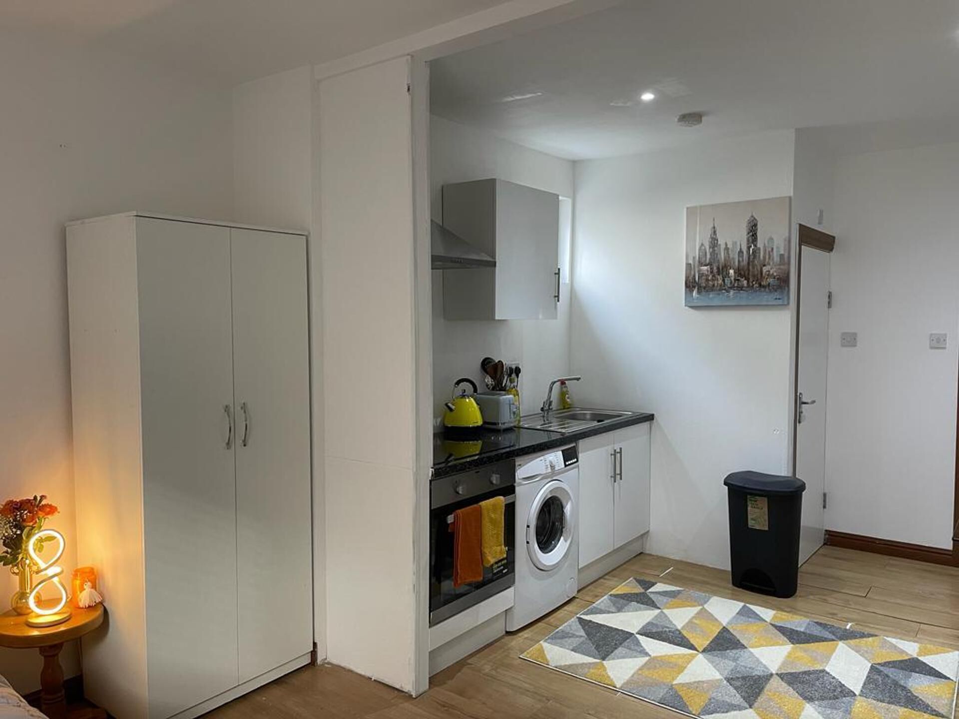 A compact kitchen with white cabinets, a washing machine, a sink, and a patterned rug.