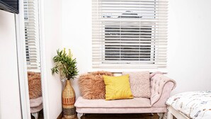 Una habitación con sofá, espejo, ventana con persianas, cesta tejida y alfombra estampada.