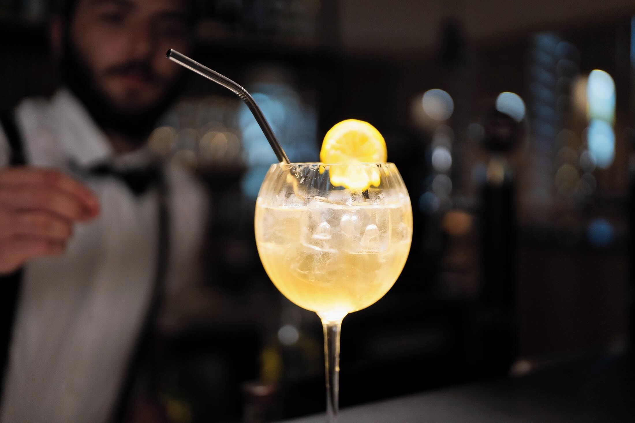 A cocktail with a lemon slice garnish and a straw, served in a glass with ice.