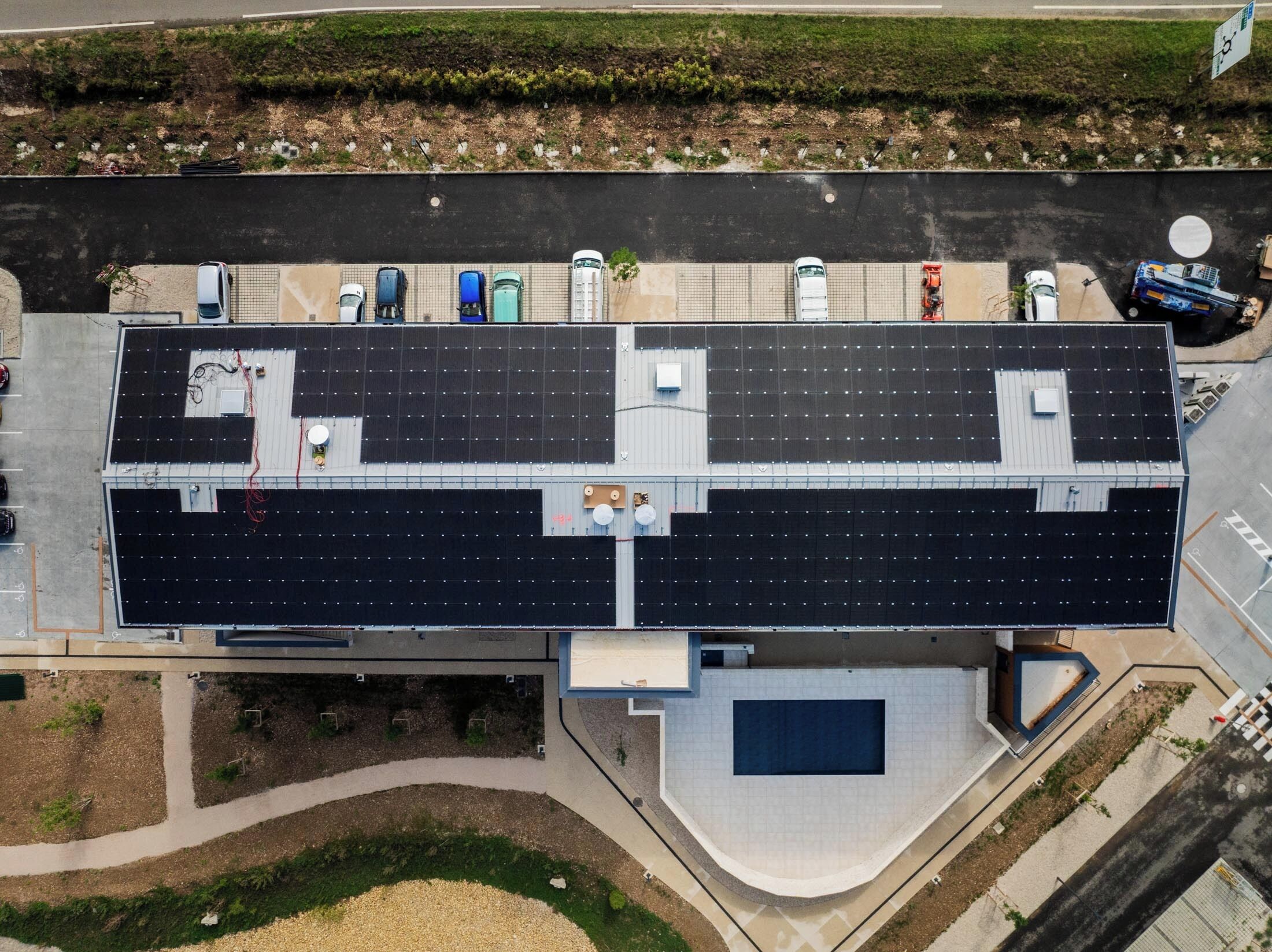 An aerial view of a building with a flat roof, solar panels, and a swimming pool.