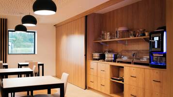 A modern kitchen with wooden cabinets, a coffee machine, and a window with a view of greenery.