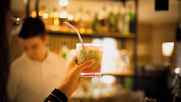 A hand holding a glass with a straw, containing a beverage with mint leaves.