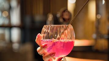 Una mano che tiene un bicchiere con una bevanda rosa e una cannuccia, appoggiato su un bancone del bar.