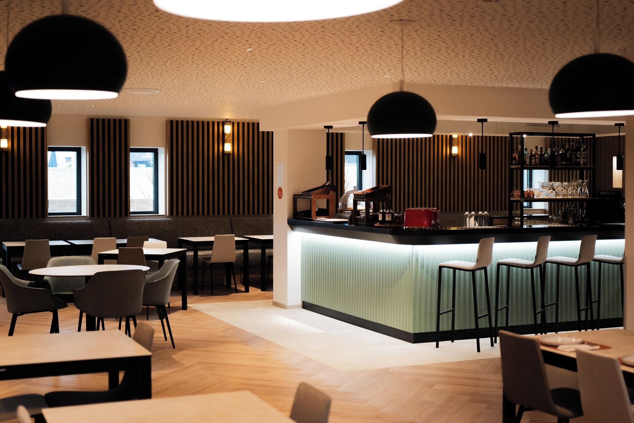 A modern bar area with a counter, stools, and a variety of bar tools.