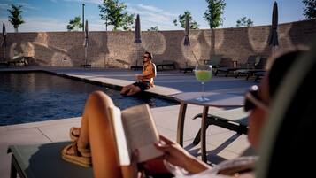 Área de piscina com espreguiçadeiras e guarda-sóis, uma parede de pedra e céu claro.