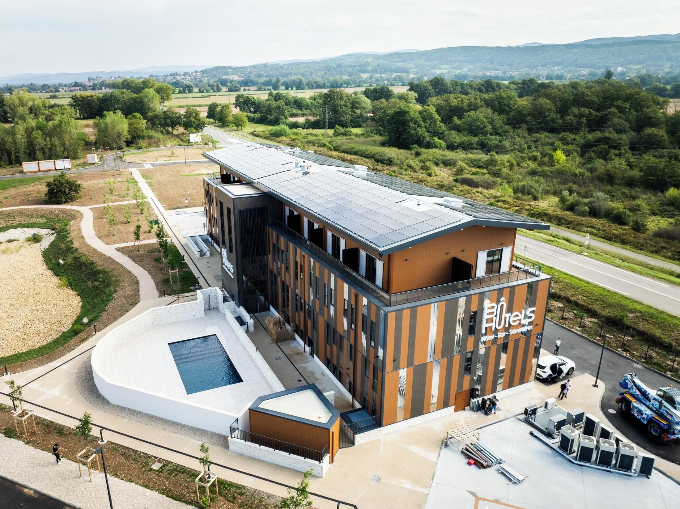 Ein modernes Hotel mit einer Solaranlage auf dem Dach, einem Schwimmbad und einem Parkplatz mit einem Servicefahrzeug.