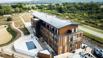 Ein modernes Hotel mit einer Solaranlage auf dem Dach, einem Schwimmbad und einem Parkplatz mit einem Servicefahrzeug.