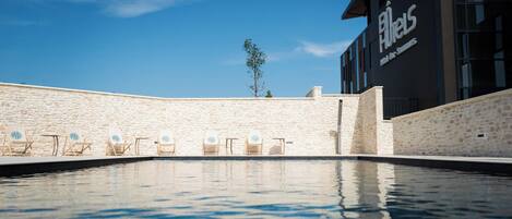 A swimming pool with lounge chairs, a stone wall, and a building with a sign reading "Hotel Big Sur."