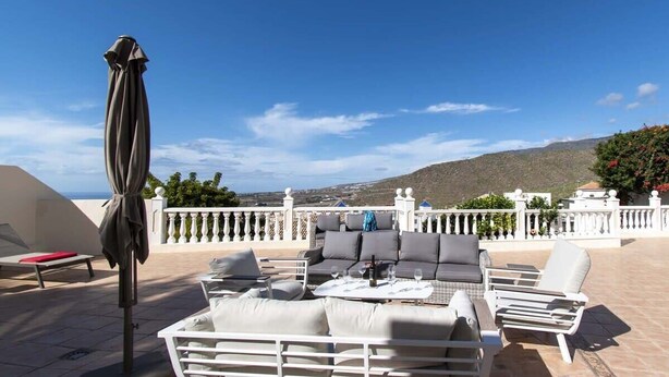 Eine Terrasse mit Sitzgelegenheiten im Freien, darunter eine Couch, Stühle und ein Tisch mit einer Flasche und Gläsern.