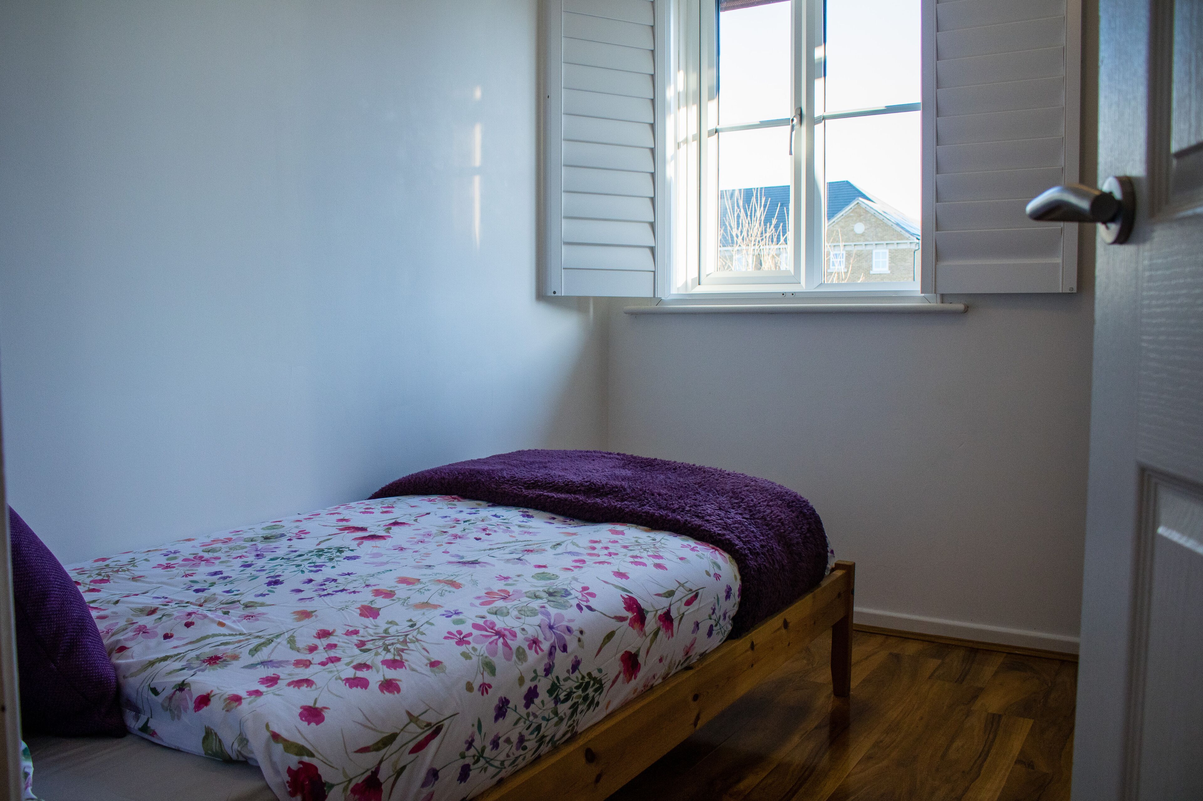 A small bedroom with a single bed, a window with shutters, and a door.
