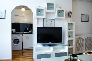 A modern kitchen with a washing machine, a dining area with a glass table, and a living area with a flat-screen TV. - Charming 2-bed Fully Furnished Apartment in London (Erith)