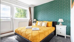 A bedroom with a large bed, two bedside tables, a window with curtains, and a green patterned wall. - Wandsworth Retreat: Spacious Quiet 2BR 2Bth Duplex + View + Nr Trains To Center! (London)