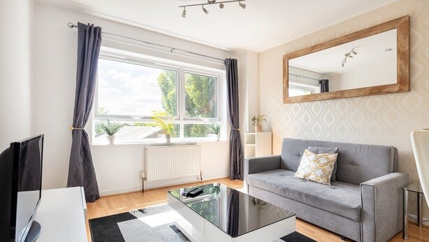 A modern living room with a grey sofa, a glass coffee table, a TV, and a large window with curtains. - Wandsworth Retreat: Spacious Quiet 2BR 2Bth Duplex + View + Nr Trains To Center! (London)