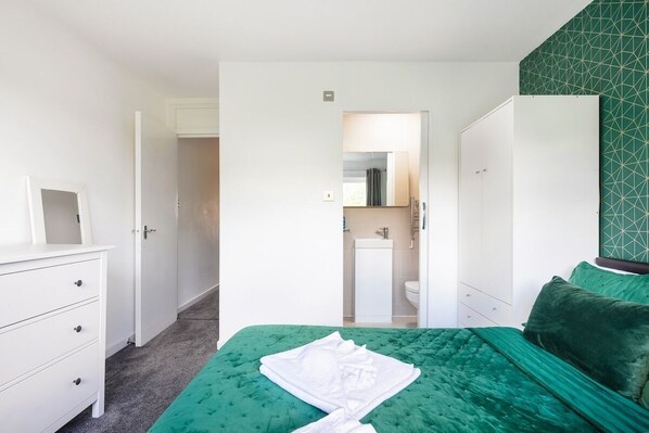 Une chambre d’hôtel avec un lit vert, une commode blanche et une salle de bain visible à travers une porte ouverte.