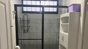 Une salle de bain compacte avec une douche à parois de verre, des toilettes et un meuble de rangement blanc.