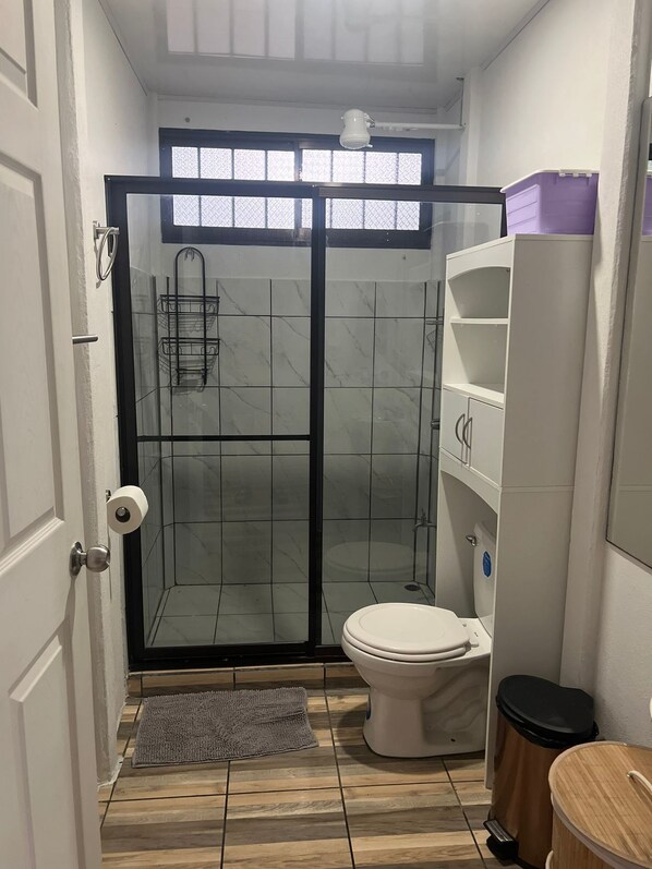 Un bagno compatto con cabina doccia in vetro, un water e un mobile contenitore bianco.