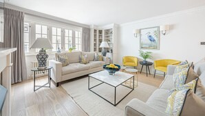 A modern living room with a sofa, coffee table, and chairs. There are bookshelves and a painting on the wall. - Elegant 4-Bedroom London Residence in Prestigious Belgravia (London)