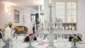 A dining area with a white table set for a meal, featuring clear glassware, a white candle, and floral arrangements. - Elegant 4-Bedroom London Residence in Prestigious Belgravia (London)