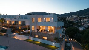 A modern multi-story residential building with a pool, outdoor seating, and a view of a cityscape.