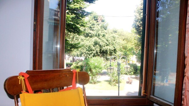 A wooden chair with a yellow cushion in front of a window with a view of a garden and trees. - Casa Ancient Charme near the sea (Levanto)