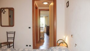 A bedroom with a bed, a chair, a bedside table with a lamp, a mirror, and a door leading to another room. - Casa Ancient Charme near the sea (Levanto)