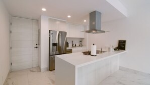 Eine moderne Küche mit weißen Schränken, einem Edelstahlkühlschrank, einem eingebauten Backofen und einer zentralen Kochinsel mit Spüle.
