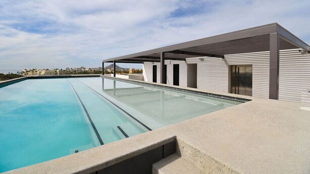 Ein moderner Poolbereich mit klarem Pool, überdachter Sitzgelegenheit und Blick auf entfernte Gebäude.