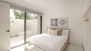 Ein modernes Schlafzimmer mit einem großen Bett, einer Schiebetür zum Balkon und zwei an der Wand befestigten Kunstwerken.