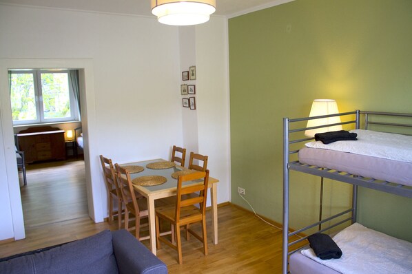A room with a bunk bed, a dining table with chairs, and a sofa.