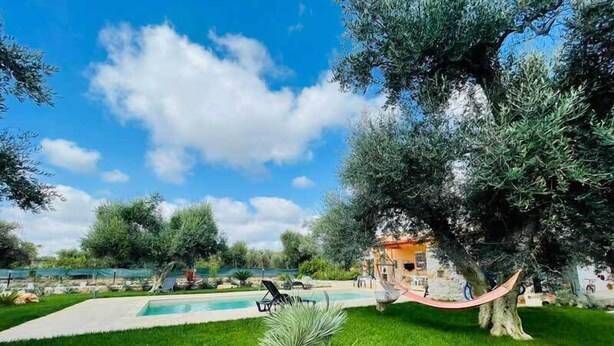 A pool area with a hammock, a large tree, and a building in the background. - 3724 All' Ombra Degli Ulivi by Barbarhouse (Latiano)