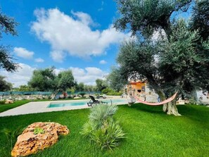 A pool area with a hammock, a large tree, and a building in the background. - 3724 All' Ombra Degli Ulivi by Barbarhouse (Latiano)