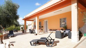 A covered outdoor seating area with lounge chairs and a table, surrounded by potted plants and a stone wall. - 3724 All' Ombra Degli Ulivi by Barbarhouse (Latiano)