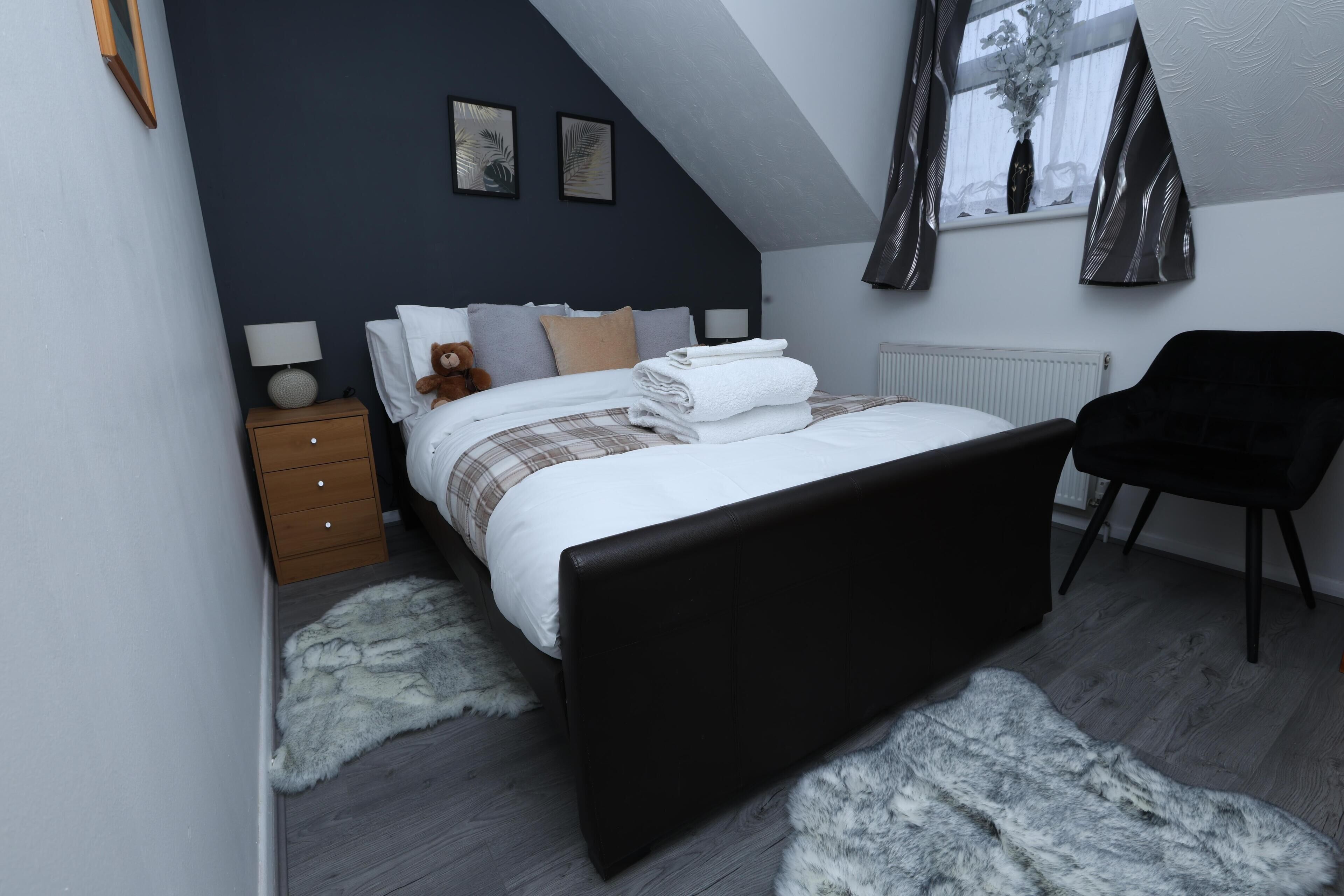 A bedroom with a bed, a nightstand, a chair, and a window with curtains.