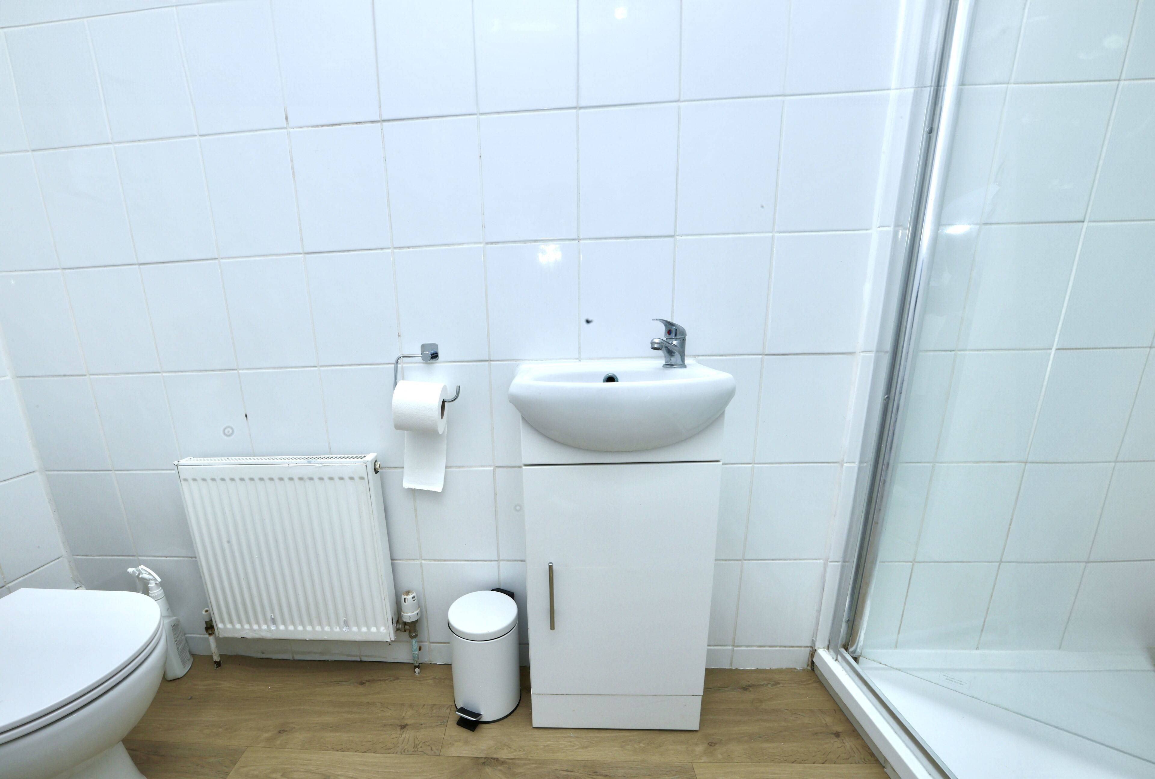 A bathroom with a toilet, a sink, a radiator, and a trash bin.