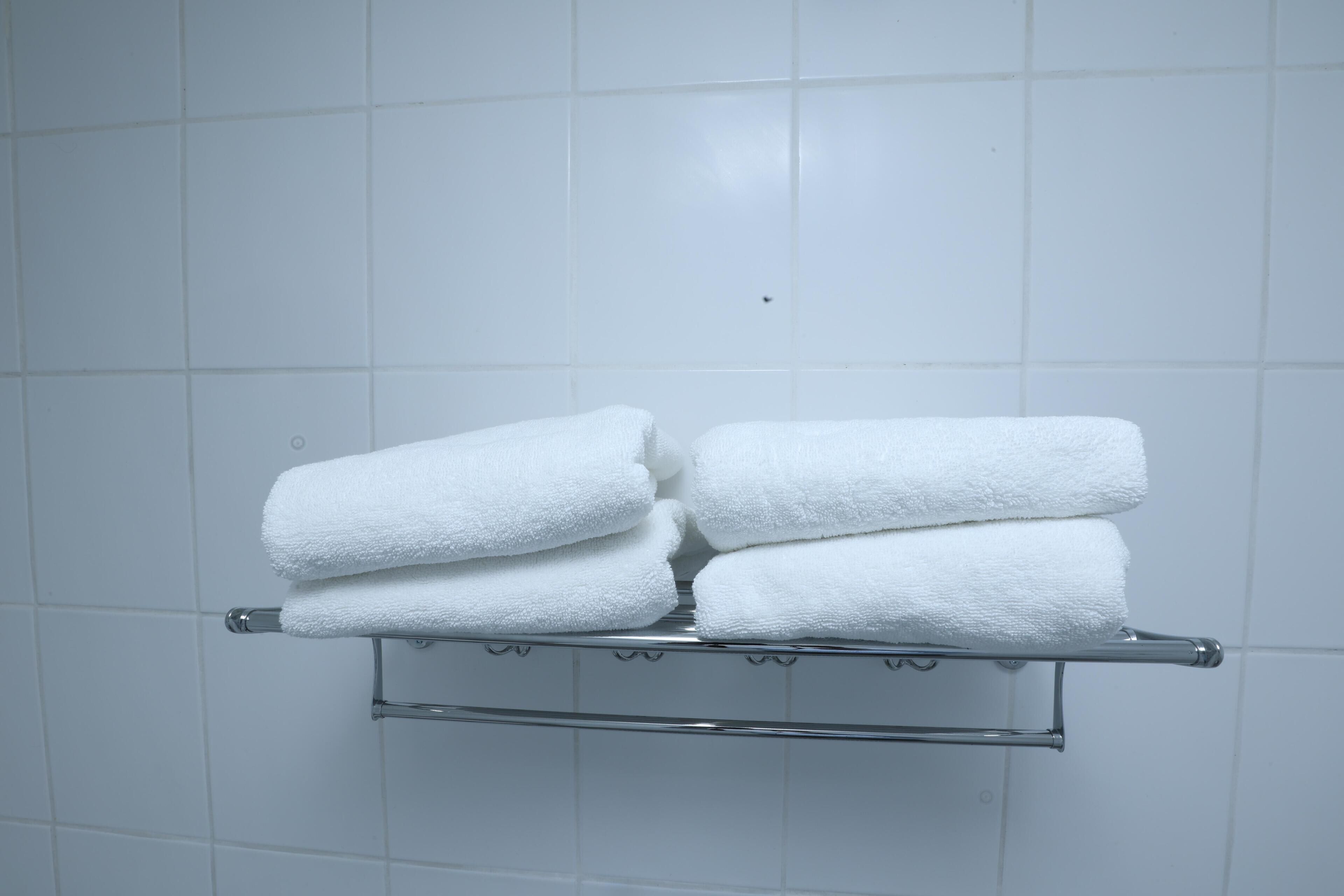 Ein Badezimmer mit weiß gefliesten Wänden und einem Metallhandtuchhalter, der drei ordentlich gefaltete weiße Handtücher trägt.