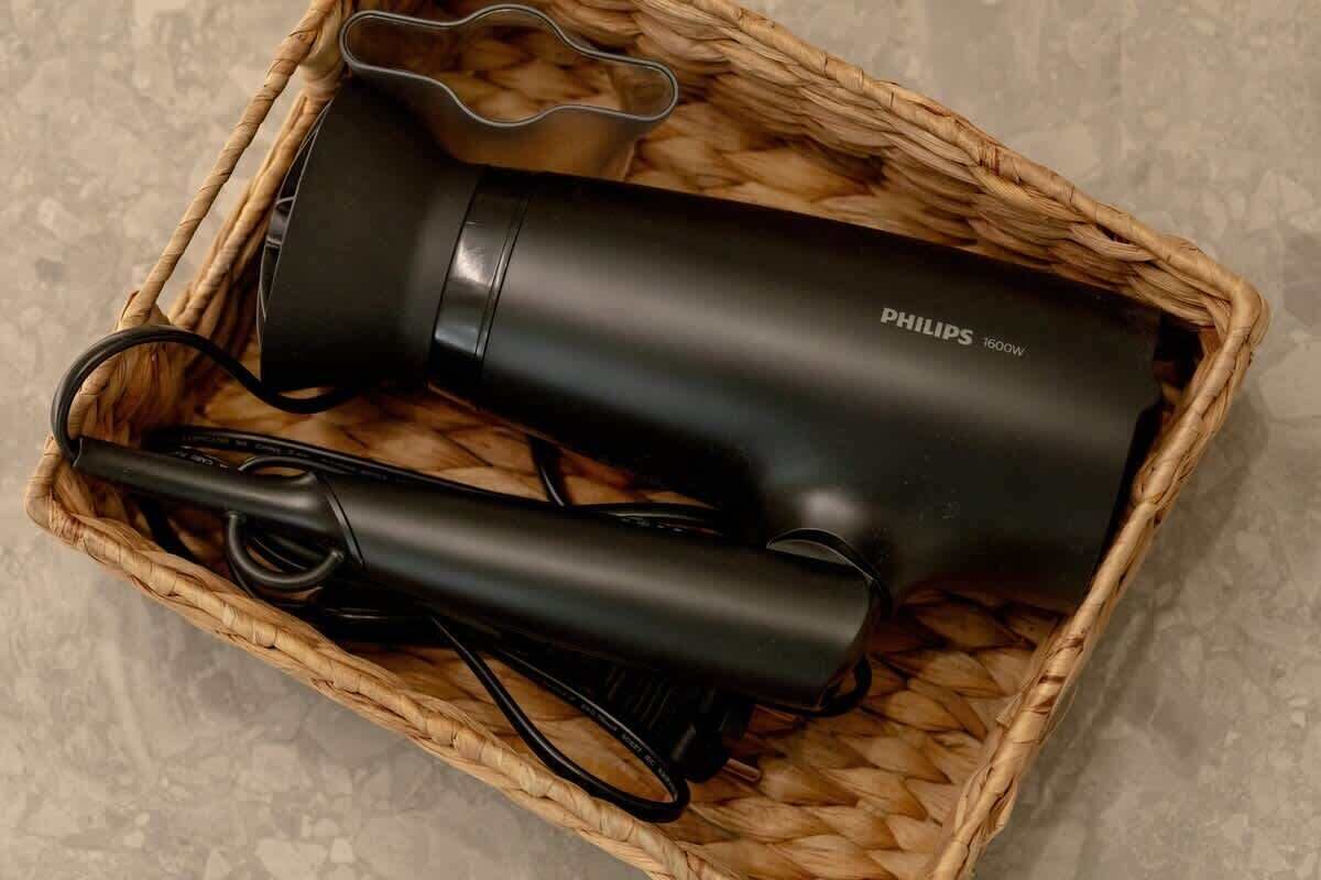 Un secador de pelo Philips y su cable de alimentación en una cesta tejida.