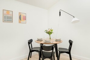 Un coin repas avec une table ronde dressée pour quatre personnes, des chaises noires, un vase avec des fleurs et deux œuvres d’art encadrées accrochées au mur.