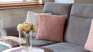 A grey sofa with two pink cushions and a vase with flowers on a round table. - Stylish Apartment with Balcony | Guaranteed Parking (Poznan)