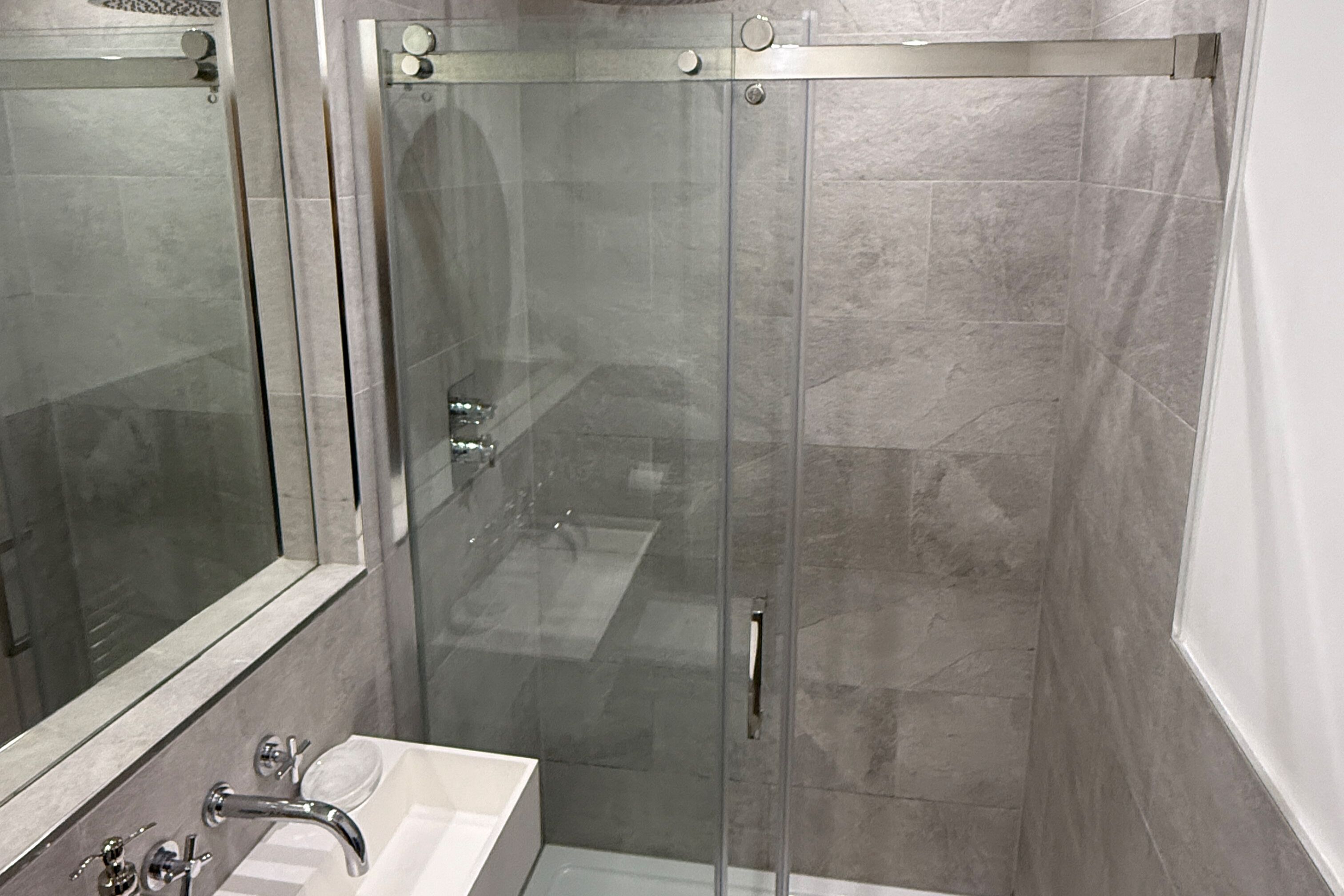 A modern bathroom with a glass shower enclosure, a large mirror, and a white sink.