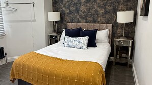 Un lit bien fait, recouvert d’une couverture de couleur moutarde, avec deux lampes de chevet et un coussin à motifs.