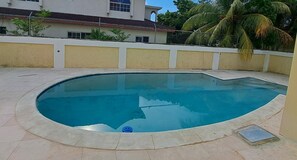 A swimming pool with a curved edge, surrounded by a low wall and a tiled floor. - Affordable Rooms at Greensview (Montego Bay)