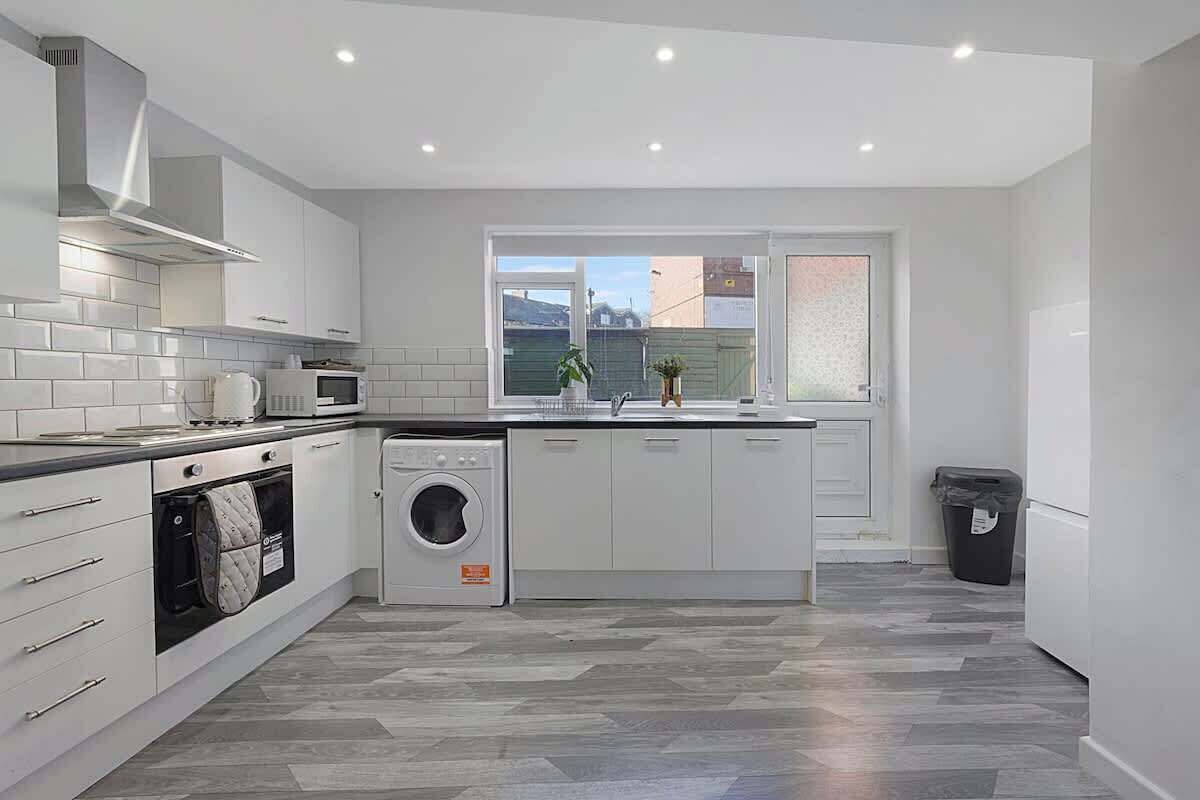 A modern kitchen with white cabinetry, a built-in oven, a washing machine, and a window with a view.