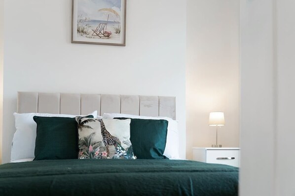 A bed with a green bedspread, two pillows, one with a giraffe print, and a headboard.
